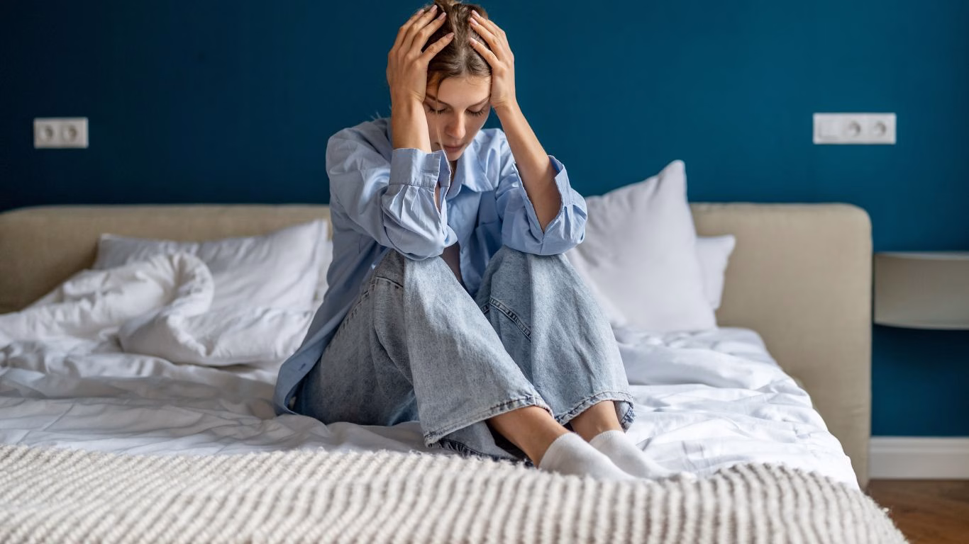 A woman sitting on a bed with her head in her hands
