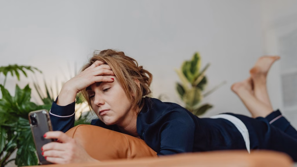 Woman lying down looking at a phone, appearing stressed