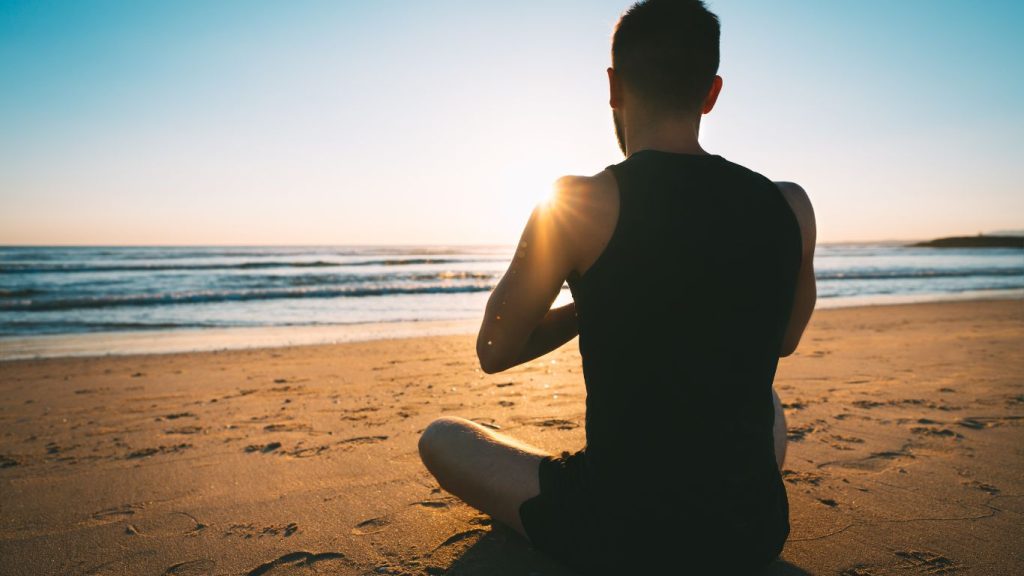 Man sitting doing somatic practice looking at the ocean