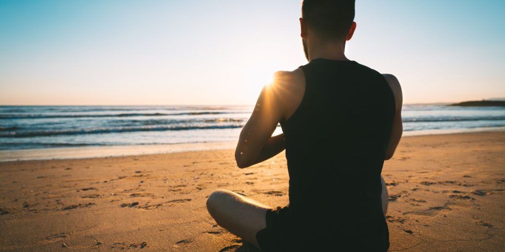 Man sitting doing somatic practice looking at the ocean