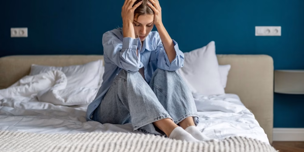 A woman sitting on a bed with her head in her hands